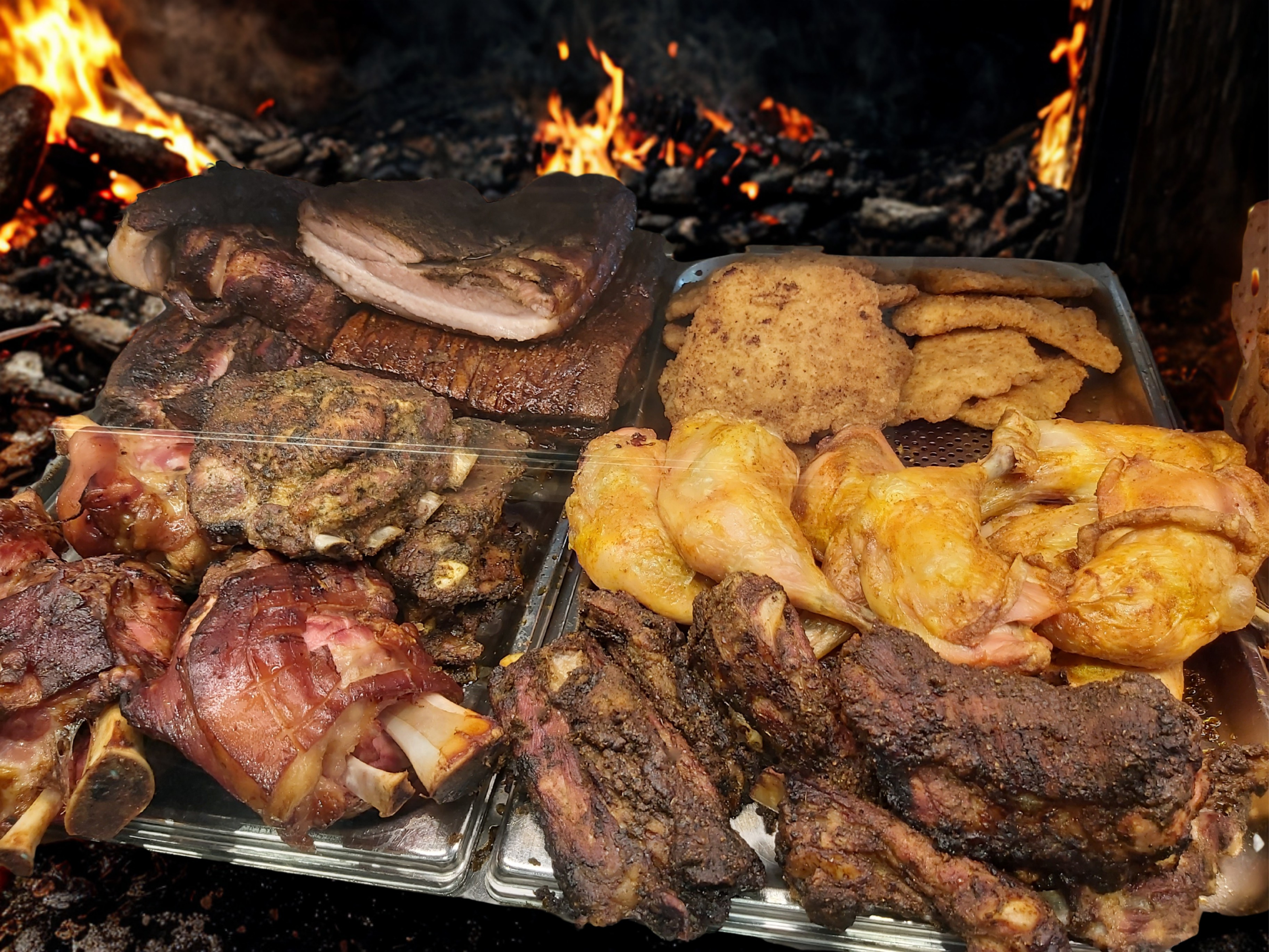 Gegrilltes Fleisch auf Platten vor einem Feuer